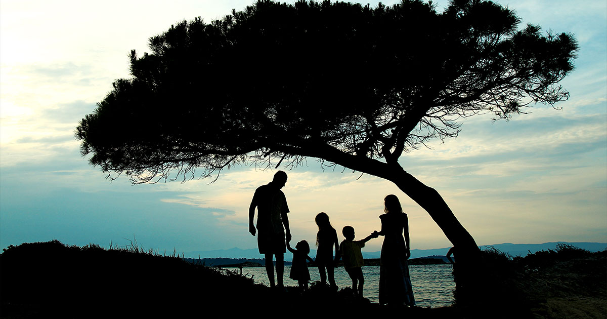 Imagen simbólica de una familia bajo un árbol junto a un lago. Representa el vínculo con las raíces del alma y lo ancestral.