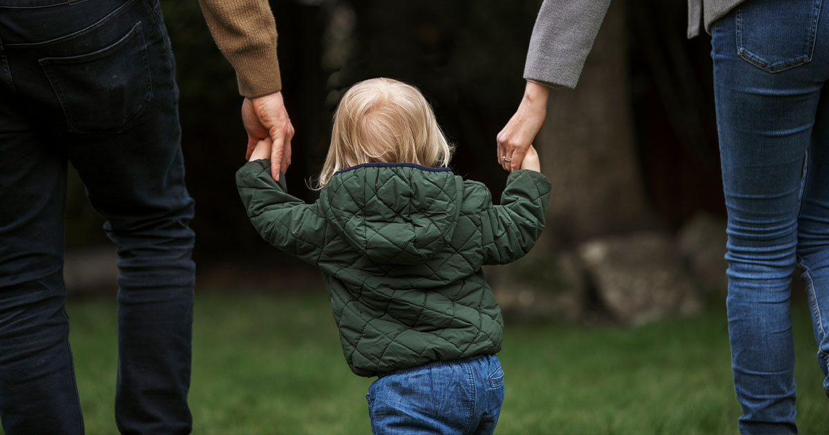 Imagen que acompaña el artículo “Tomar a los padres”. Un niño camina tomado de la mano de sus padres, simbolizando el vínculo con el origen.